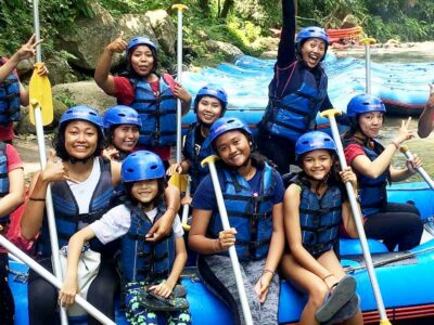 A cheerful group of rafters, children and adults alike, ready for river rafting, posing with paddles on a raft in Bali.