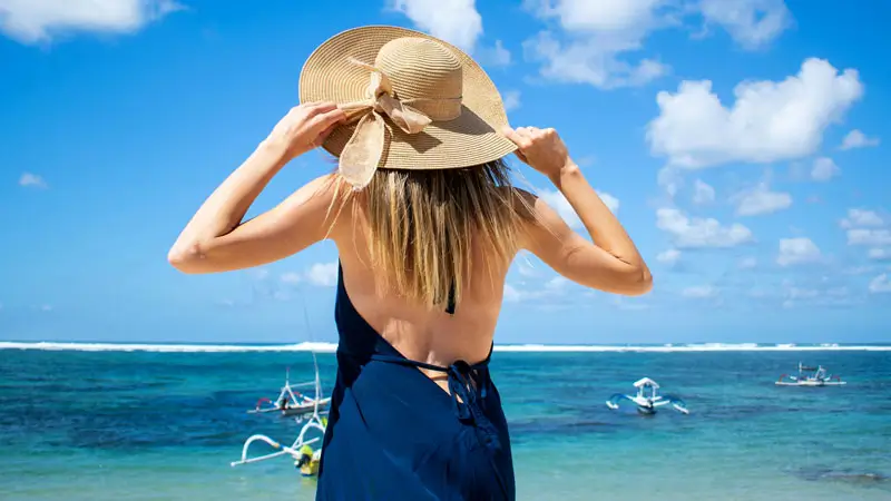 Woman enjoying ocean view at Nusa Dua Beach, Bali, with traditional boats in the background.