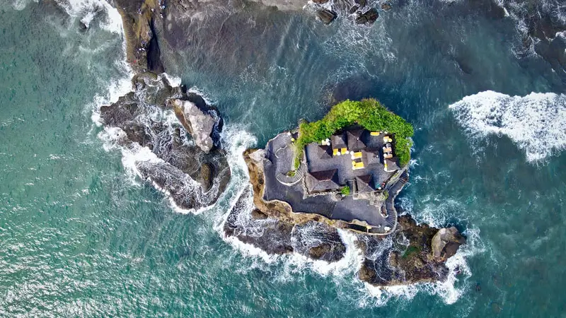 Aerial view of Tanah Lot Temple in Bali, surrounded by ocean waves on a rocky islet.