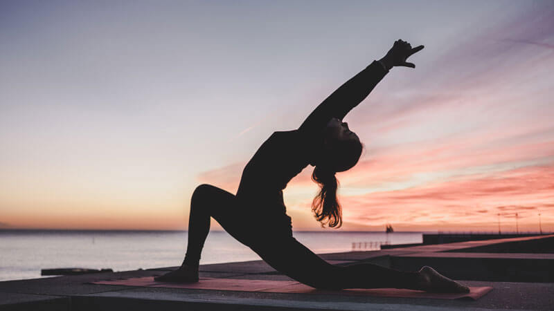 Silhouette of a woman doing yoga at sunset by the sea