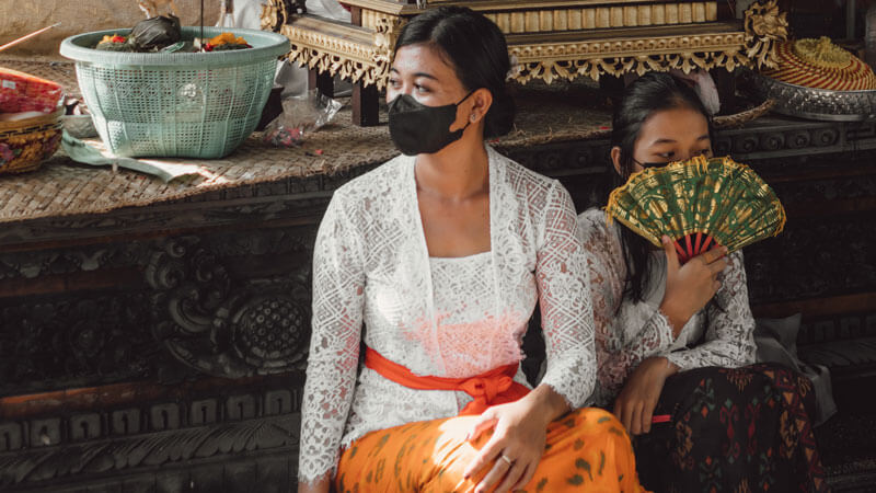 Balinese women in traditional attire with face masks at a temple