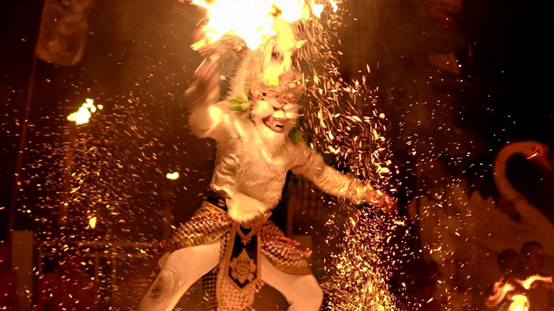 Performer in Hanoman costume at Melasti Beach Kecak Dance, emitting sparks during a dramatic fire dance scene.