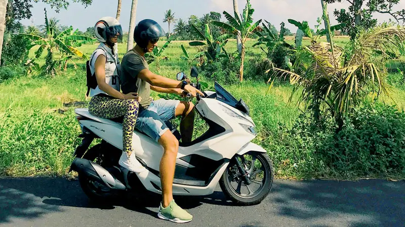 Couple riding a motorbike through the scenic countryside in Bali during their honeymoon.