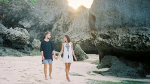 Couple walking hand-in-hand on a serene beach in Bali during sunset.