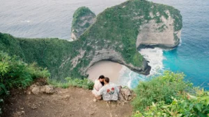 Couple enjoying a romantic view overlooking Kelingking Beach in Bali, a perfect spot for honeymooners and romantic getaways.