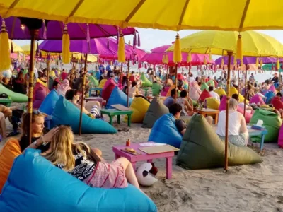 Colorful umbrellas and beanbags on Seminyak Beach, with visitors enjoying the vibrant sunset scene.