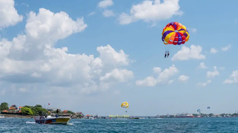 Couple parasailing over the clear blue waters of Tanjung Benoa, a hub for watersports and adventure in Bali.