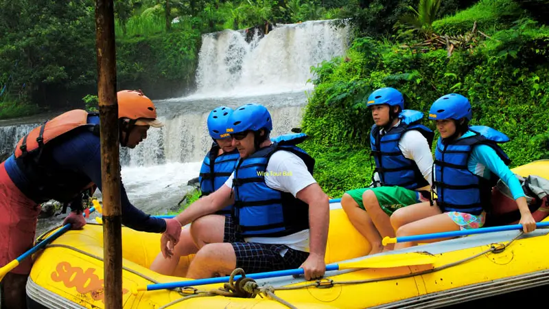 Rafting guide assisting tourists with safety gear before starting Jungle River Rafting in East Bali.