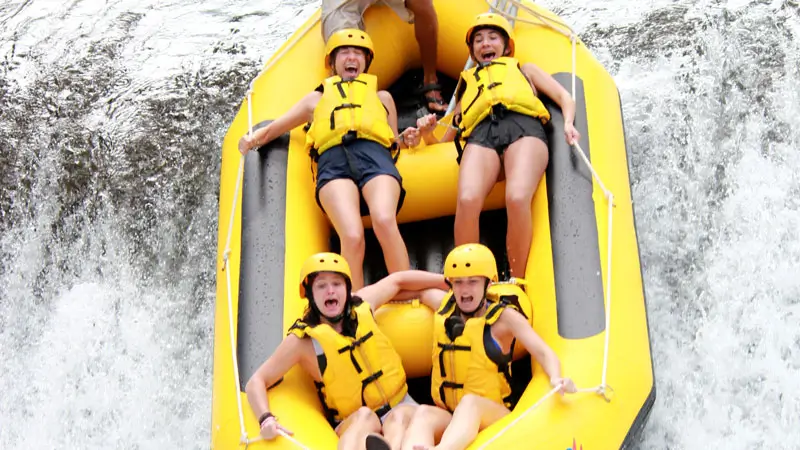 Excited tourists rafting down a waterfall on Telaga Waja River in Bali, experiencing an adrenaline-pumping whitewater adventure.