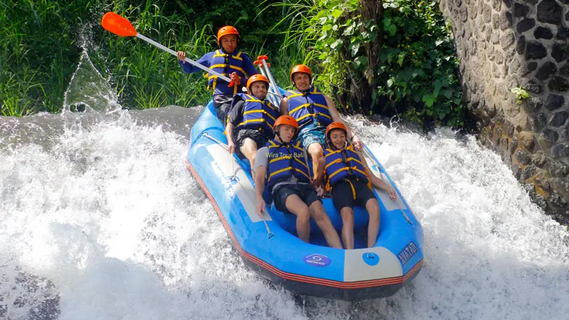 Group of tourists rafting down a waterfall on Telaga Waja River in Bali, wearing life jackets and helmets for a thrilling whitewater experience.