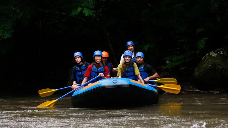 Group of happy tourists enjoying whitewater rafting on the Ayung River in Bali, wearing helmets and life jackets for a safe and thrilling adventure.